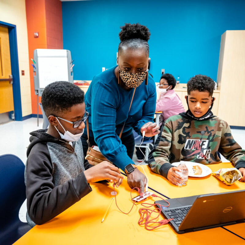 Teacher working with 2 kids and a laptop with snacks